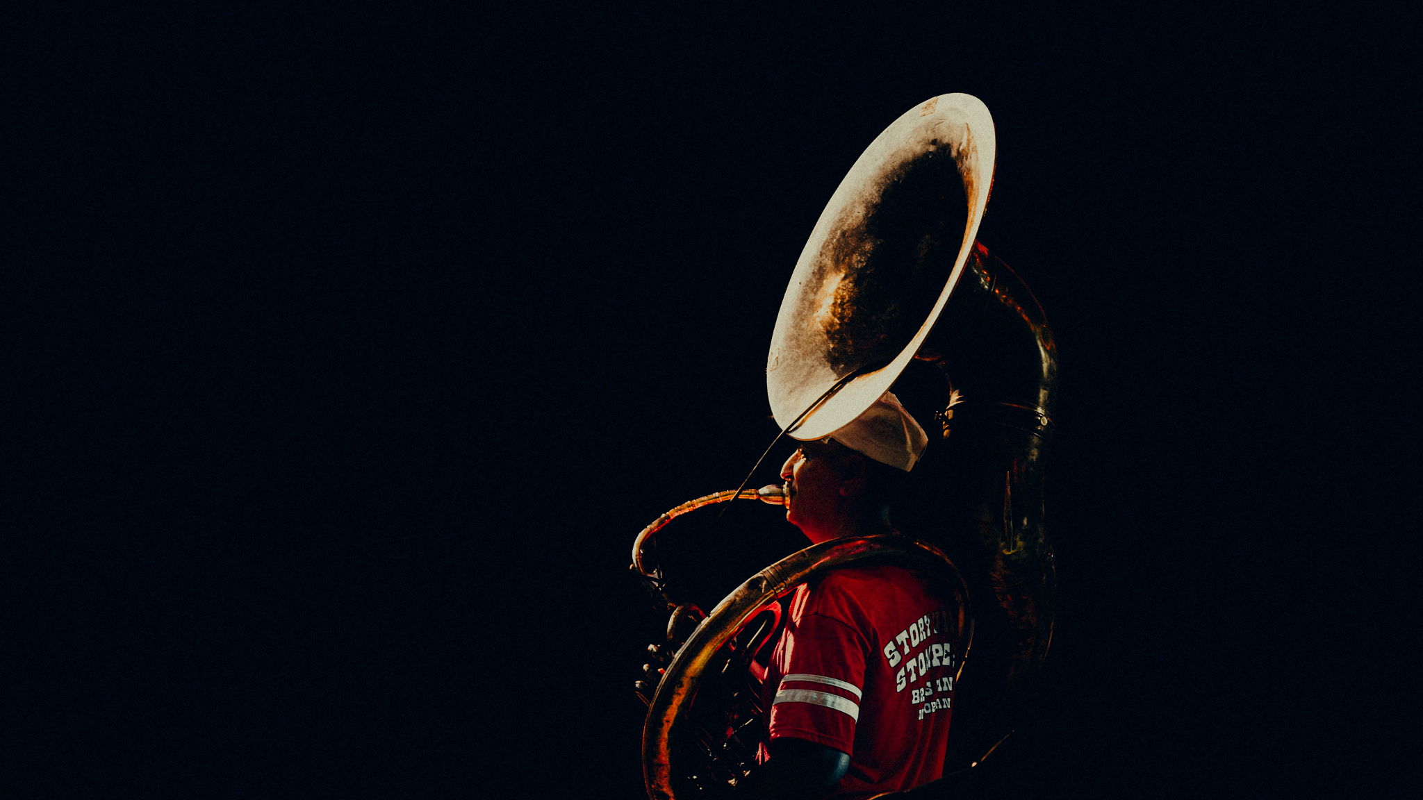 Sousaphone player illuminated against a dark stage