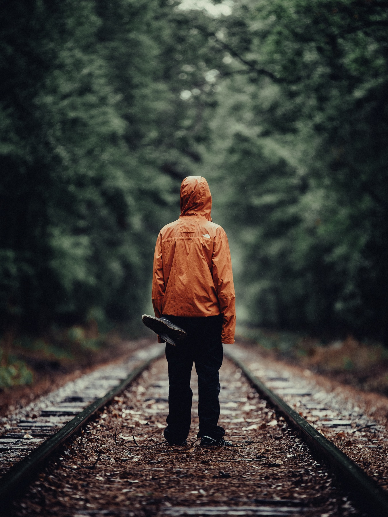 Figure in an orange rain jacket on forest railway tracks
