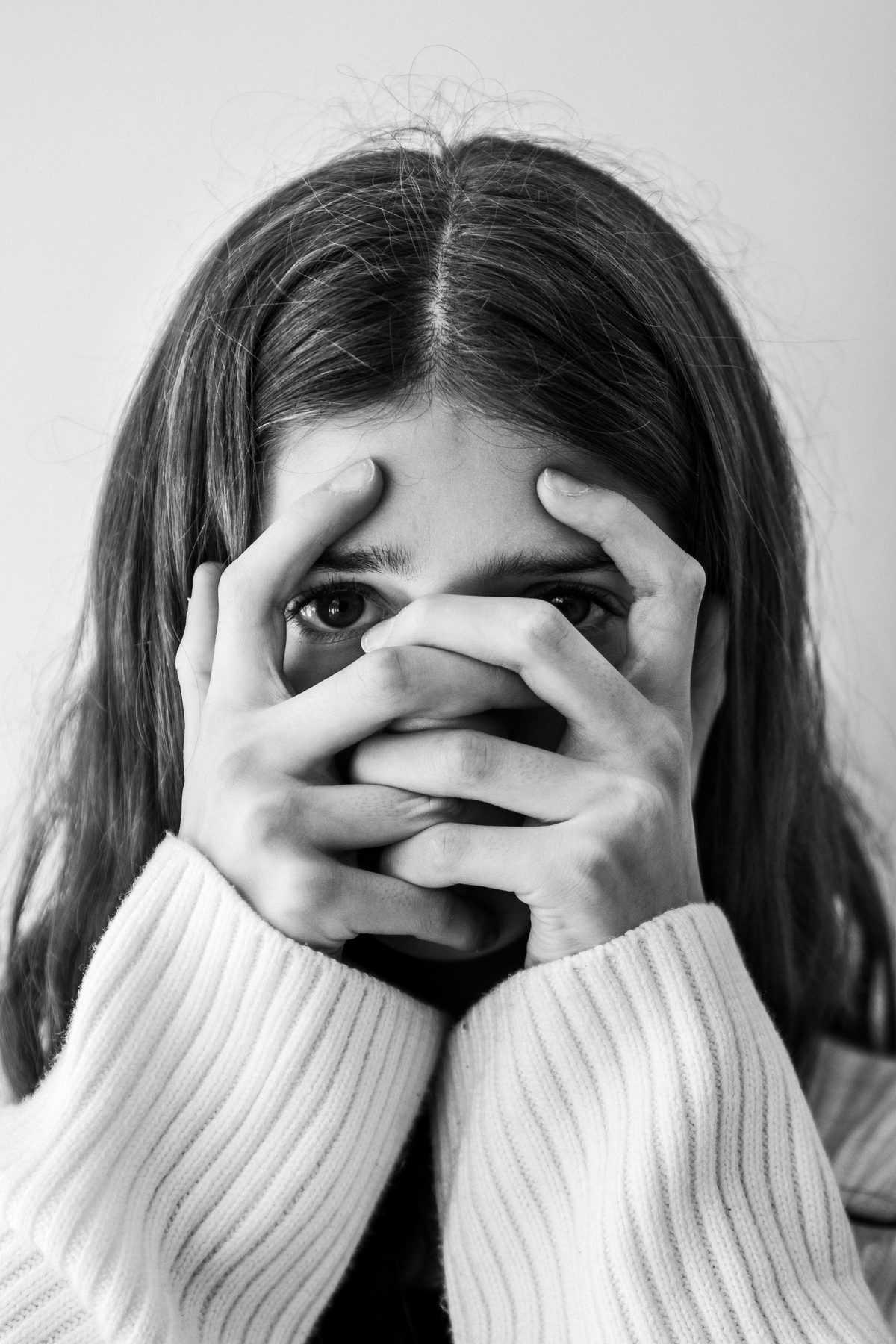 Hands covering the face, eyes showing through