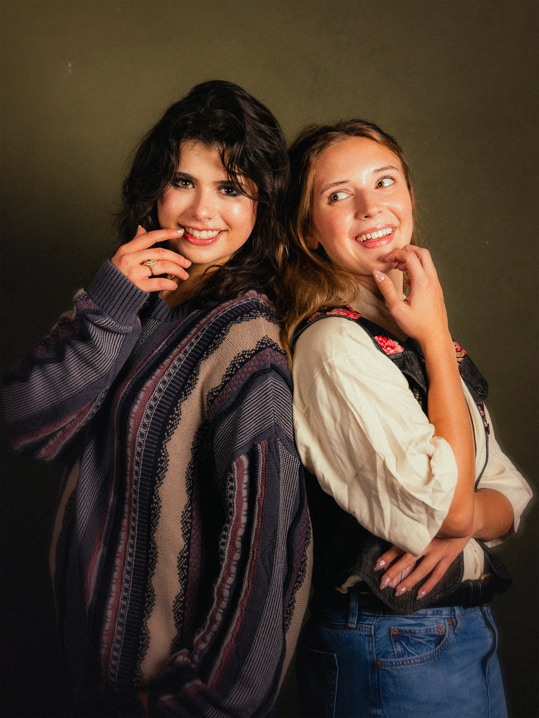 Two people posing back to back against an olive studio backdrop